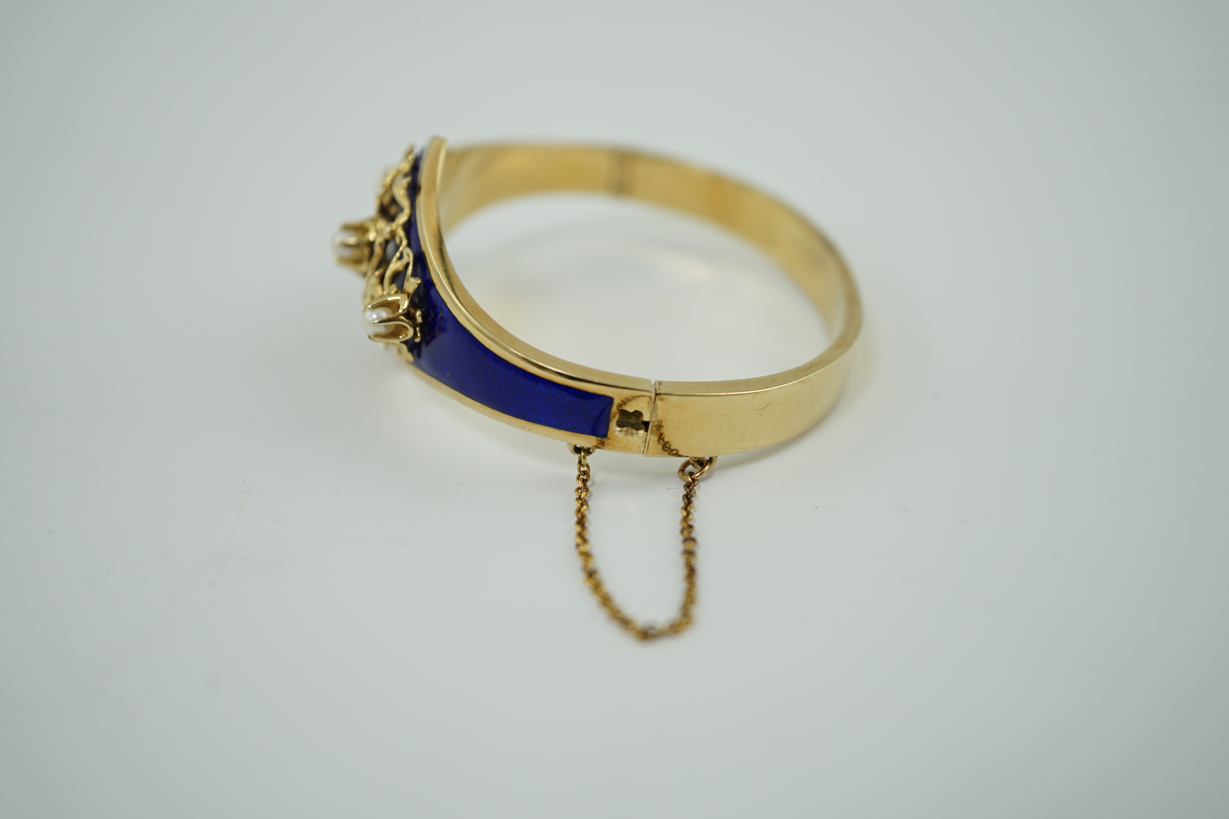 A continental Victorian style 14k gold, blue guilloche enamel and three stone cultured pearl set hinged bangle